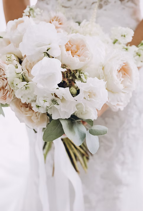 young girl in a white wedding dress holds in her hands a bouquet of flowers and greenery